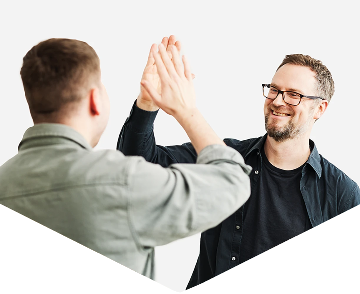 Zwei Kollegen feiern eine erfolgreiche Zusammenarbeit und geben sich motiviert ein High Five in einem Coworking Space in München.