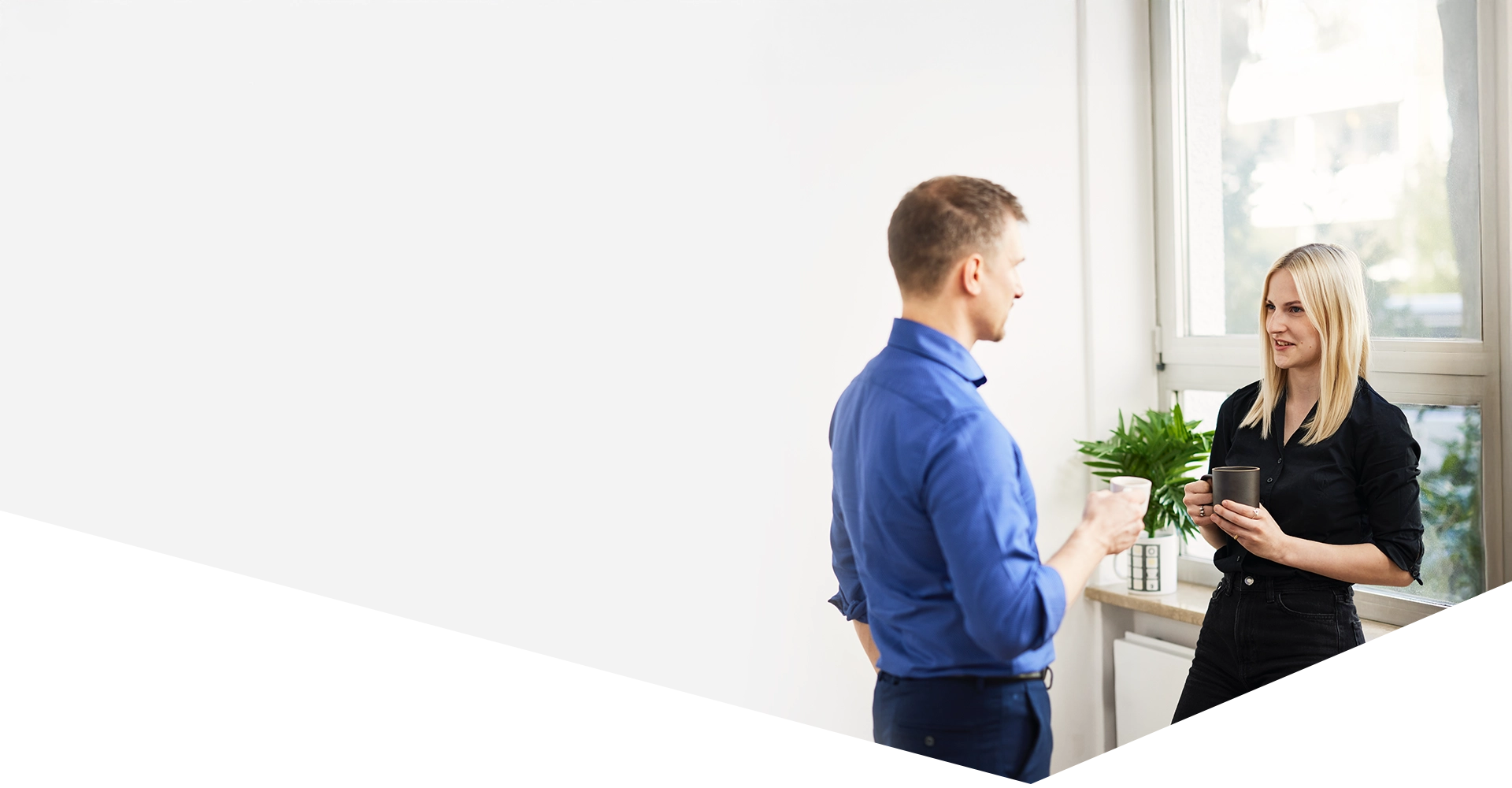 Zwei Kollegen unterhalten sich bei einer Tasse Kaffee in einem modernen Büro in München mit Blick auf die Stadt, was für eine offene Unternehmenskultur und angenehme Arbeitsatmosphäre spricht.