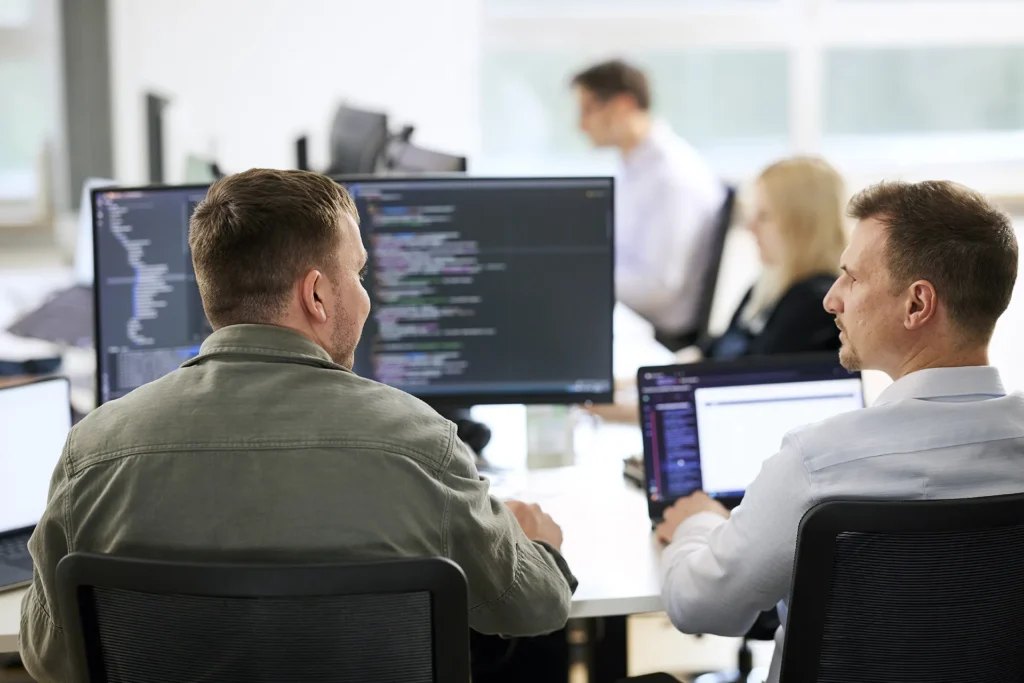 Zwei Entwickler diskutieren über Code auf einem Laptop in einem modernen Büro